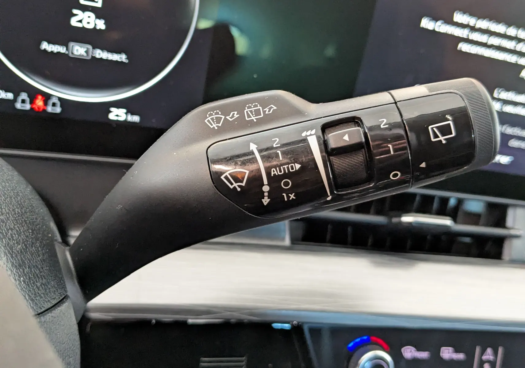 Gros plan sur la commande des essuie-glaces du Kia Sportage blanc 2025, avec tableau de bord numérique en arrière-plan.