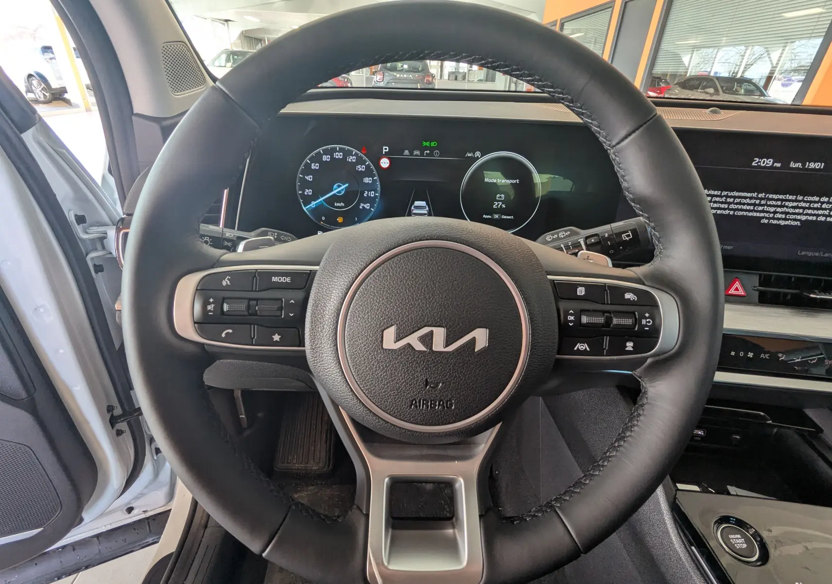 Vue intérieure centrée sur le volant noir du Kia Sportage blanc 2025 avec tableau de bord digital et écran tactile.