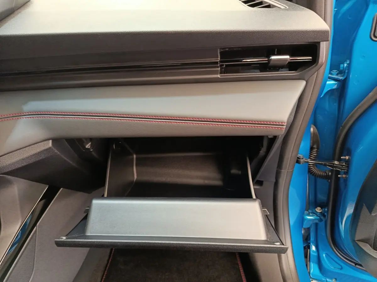 Vue intérieure côté passager du Ford Puma bleu 2025, boîte à gants ouverte avec surpiqûres rouges sur le tableau de bord.