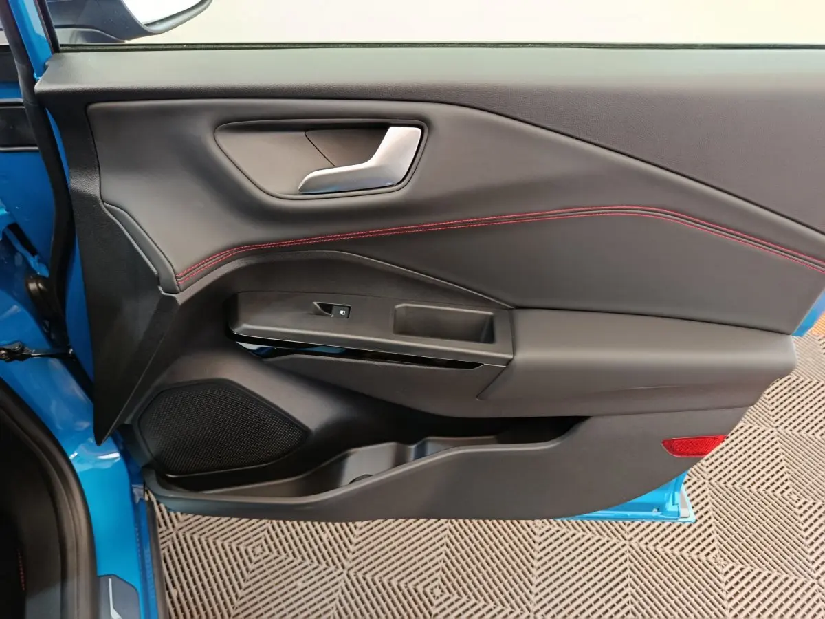 Vue rapprochée de la porte avant gauche bleu vif du Ford Puma 2025, avec surpiqûres rouges et poignée argentée.