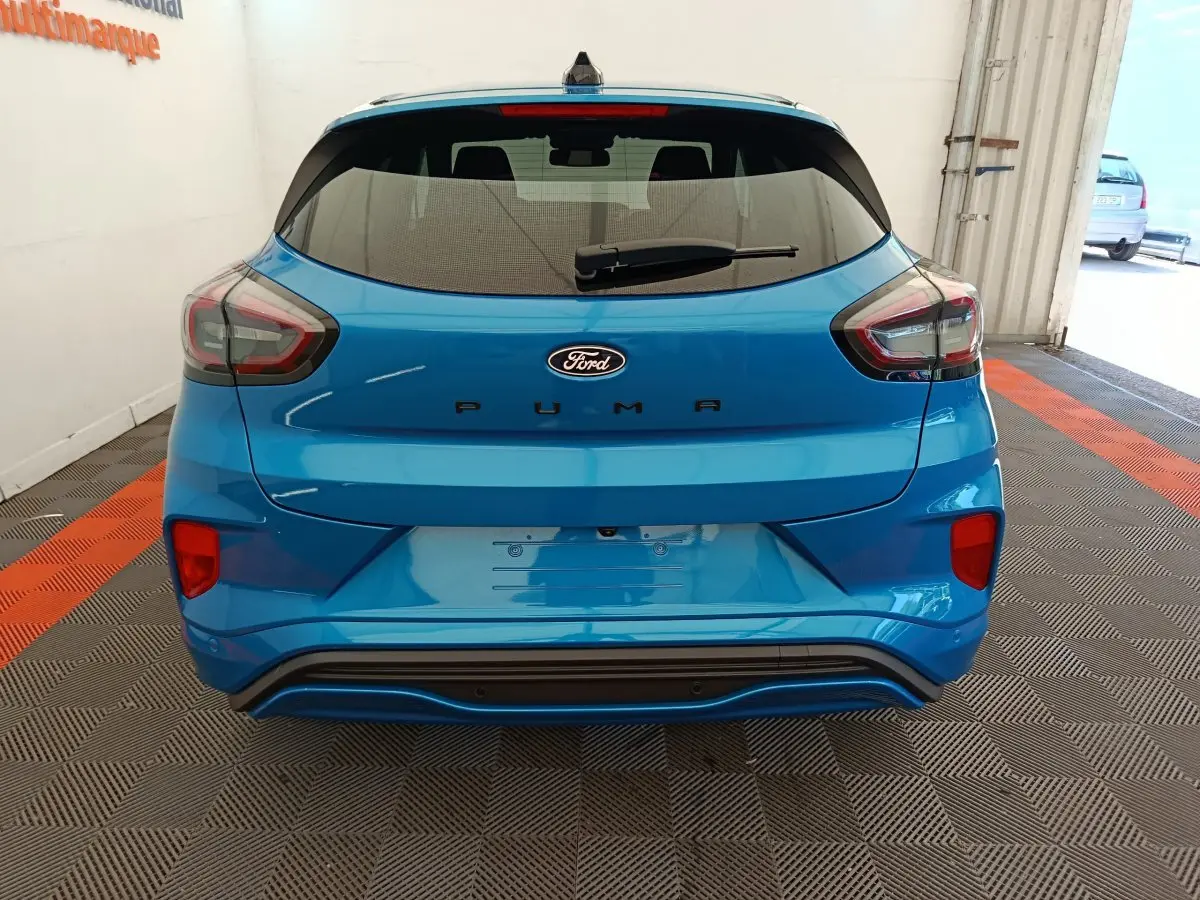 Vue arrière d'une Ford Puma bleu vif 2025 avec feux arrière LED et hayon fermé dans un garage.