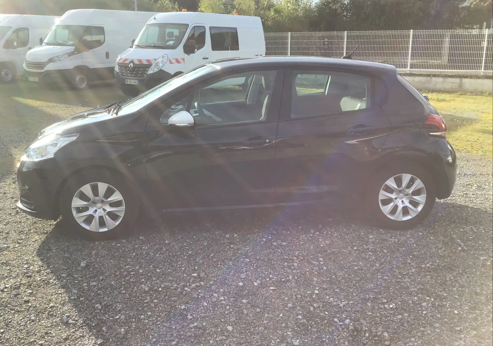 Peugeot 208 1.2 PureTech 68 essence vue de profil côté gauche, couleur noire, sur un sol gravillonné en extérieur.
