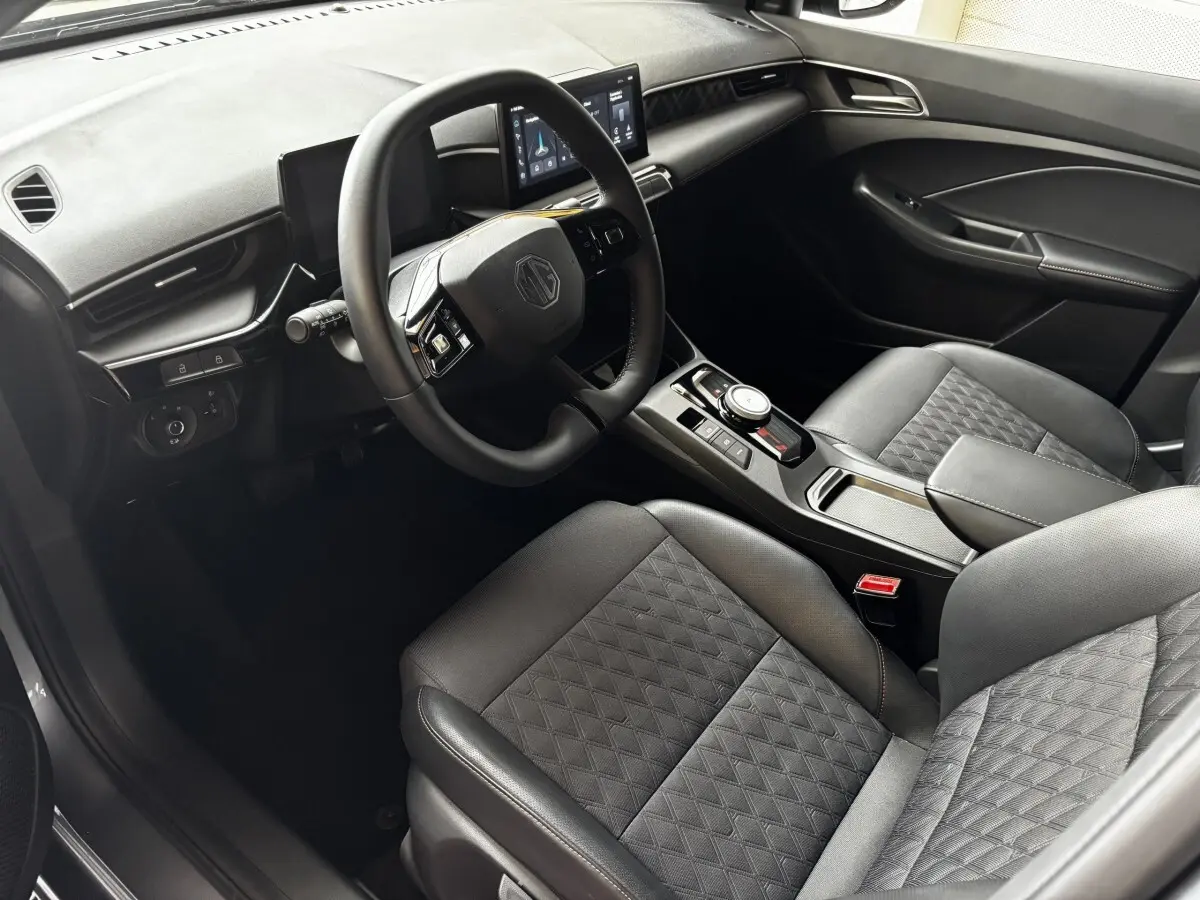 Intérieur de MG3 1.5L Hybrid+ Luxury 2025 vu côté conducteur, volant suede multifonctions et sièges gris matelassés.