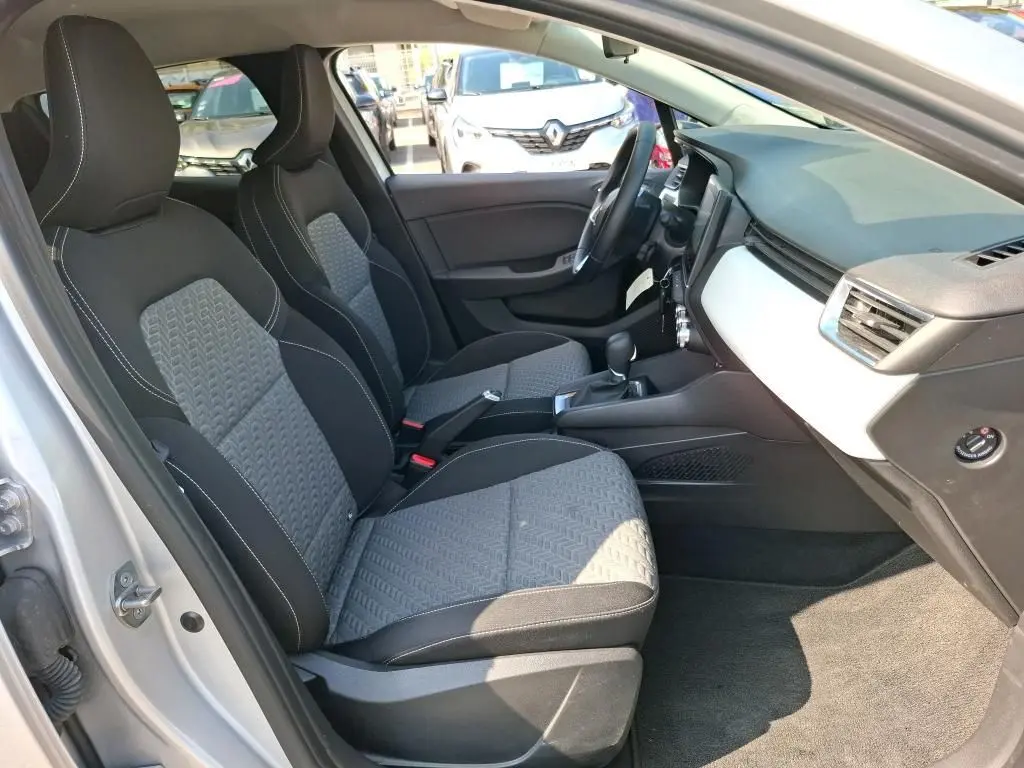 Vue intérieure côté conducteur de la Renault Clio gris platine 2023, sièges tissu bicolore et tableau de bord clair.