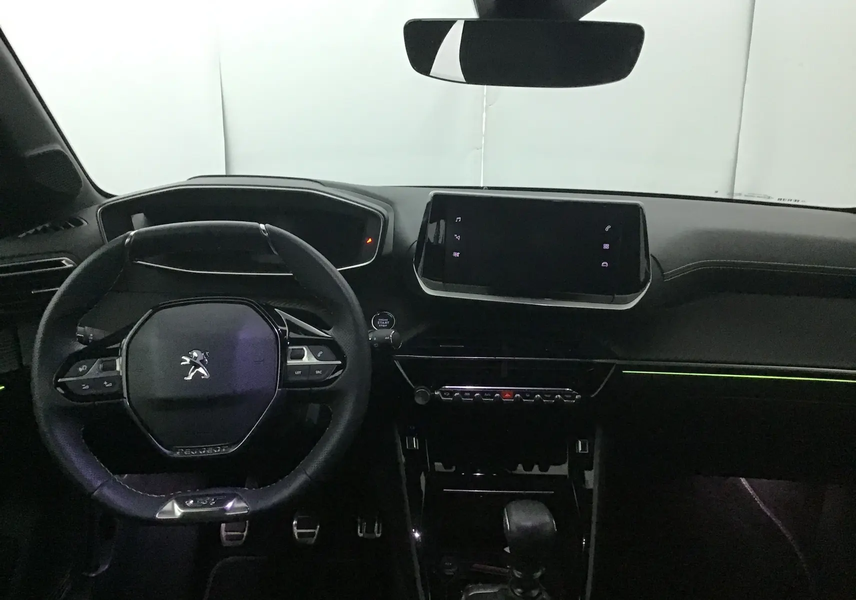 Intérieur Peugeot 208 2023 vue du poste de conduite, volant compact et écran tactile central, ambiance sombre avec éclairage d’ambiance.