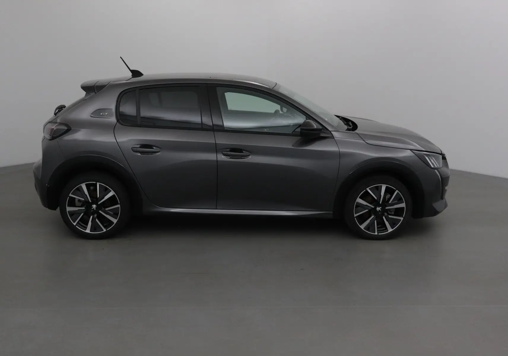Profil côté gauche d'une Peugeot 208 1.2 PureTech 100 GT S&S gris platinium avec jantes alliage noires et logo GT visible.