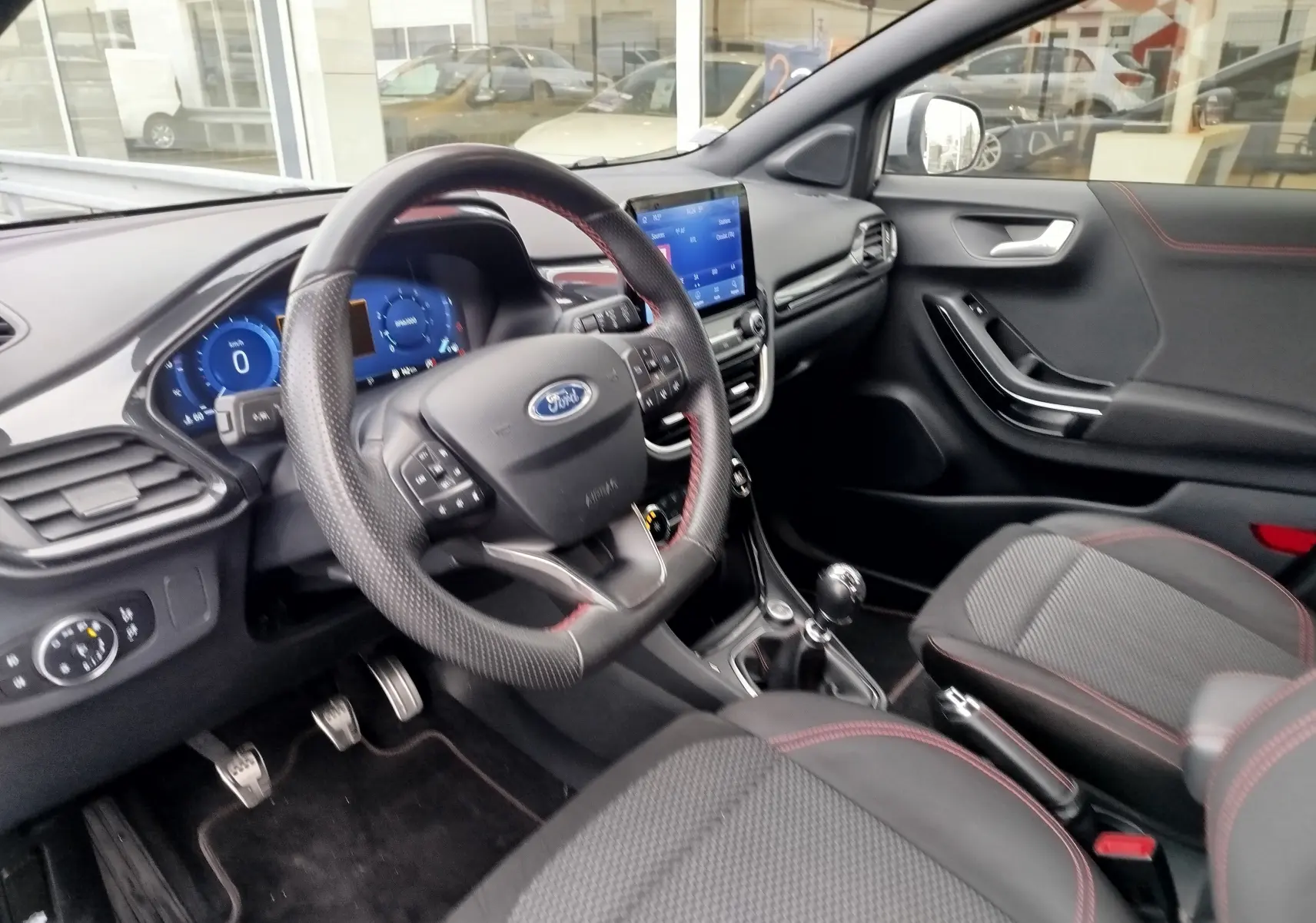 Intérieur avant droit du Ford Puma 1.0 EcoBoost 2021 avec volant cuir perforé et surpiqûres rouges, console tactile visible.