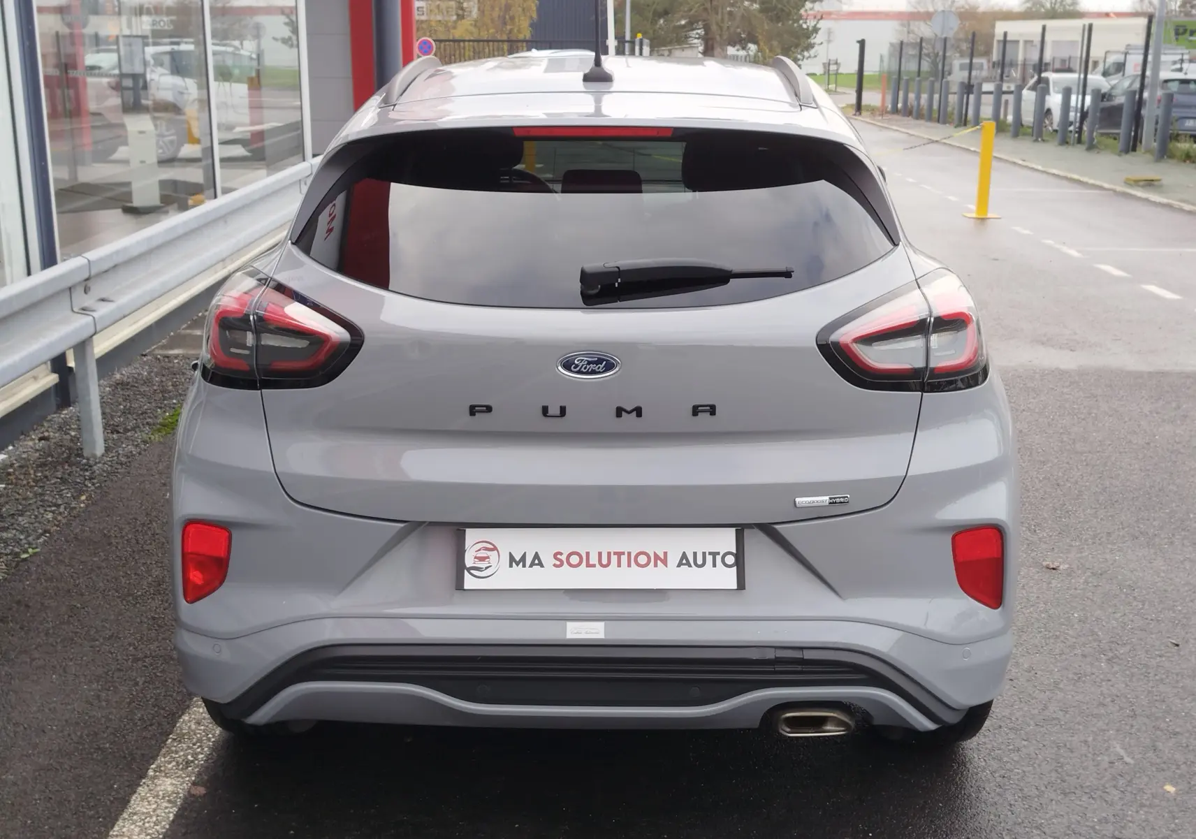 Vue arrière d'une Ford Puma 1.0 EcoBoost gris mat avec feux LED et sortie d'échappement visible sur un parking.
