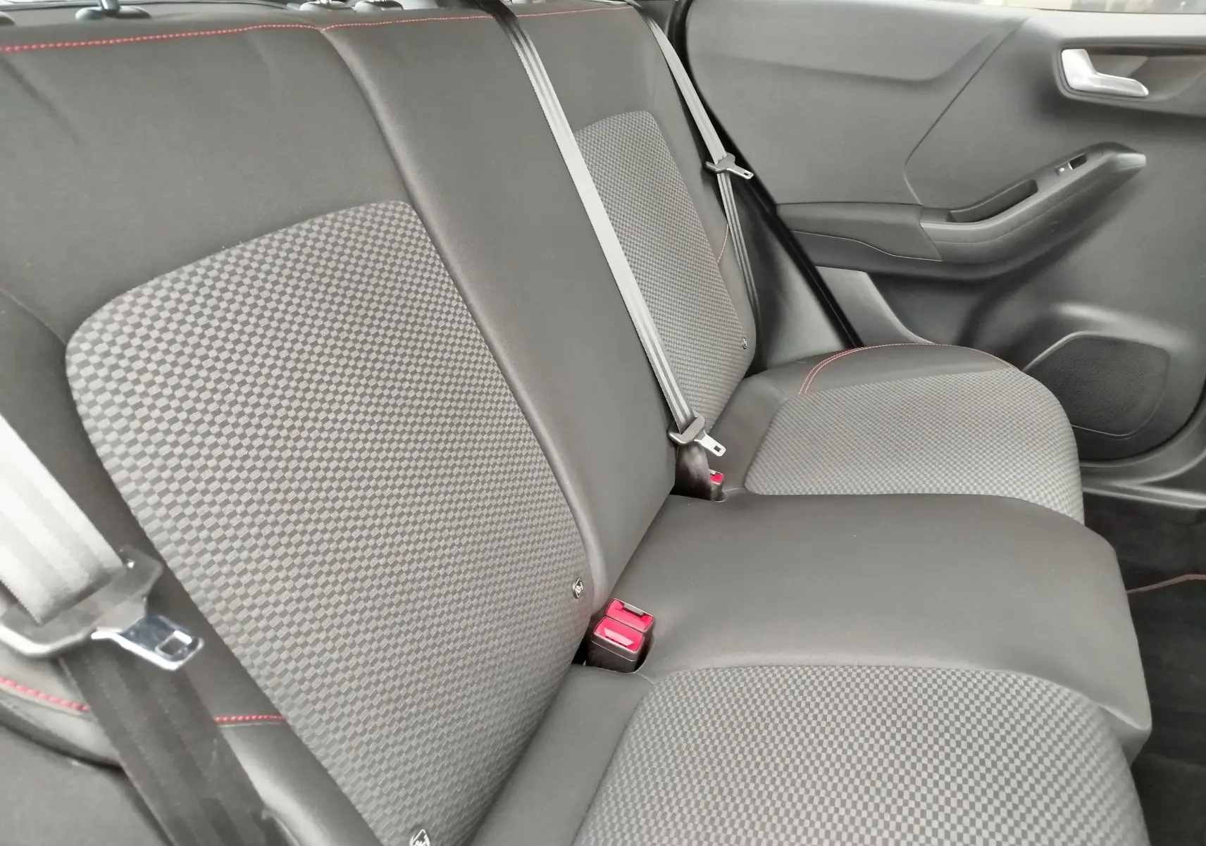 Vue intérieure du siège arrière droit du Ford Puma 2021, tissu gris à motifs avec surpiqûres rouges et ceinture de sécurité.