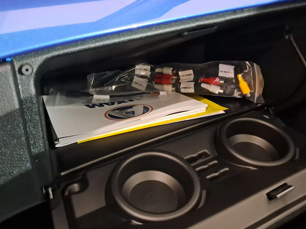 Coffre ouvert de l'AIXAM AMBITION bleu 2026 montrant des manuels et câbles, avec porte-gobelets intégrés.