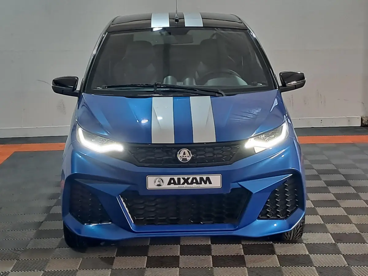 Vue avant d'une Aixam Ambition 2026 bleu avec bandes blanches, phares allumés et rétroviseurs noirs.
