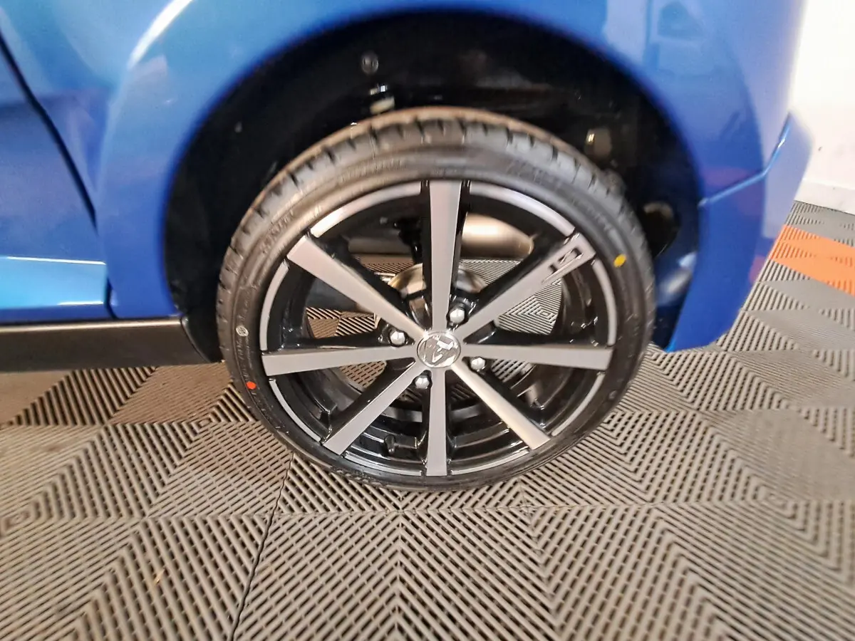 Gros plan sur la roue avant droite de l'AIXAM AMBITION bleue, mettant en valeur la jante noire à branches fines.