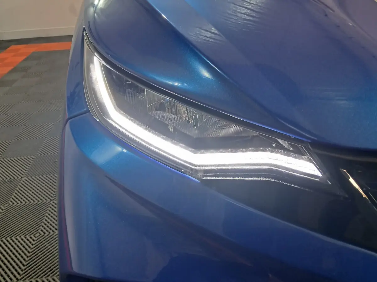 Gros plan sur le phare avant gauche allumé d'une Aixam Ambition bleu métallisé 2026, avec carrosserie lisse et brillante.