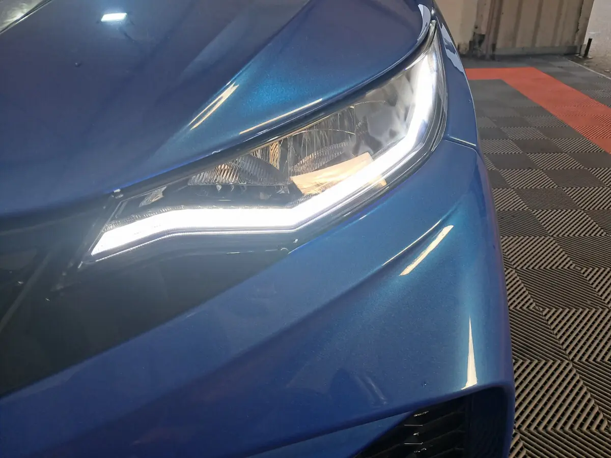 Gros plan sur le phare avant droit bleu métallisé de l'AIXAM AMBITION 0.5 CITY GTO avec éclairage LED allumé.