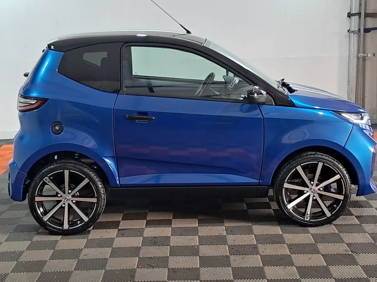 Vue de profil côté gauche d'une Aixam Ambition 2026 bleu avec jantes noires et rétroviseur caméra côté conducteur.