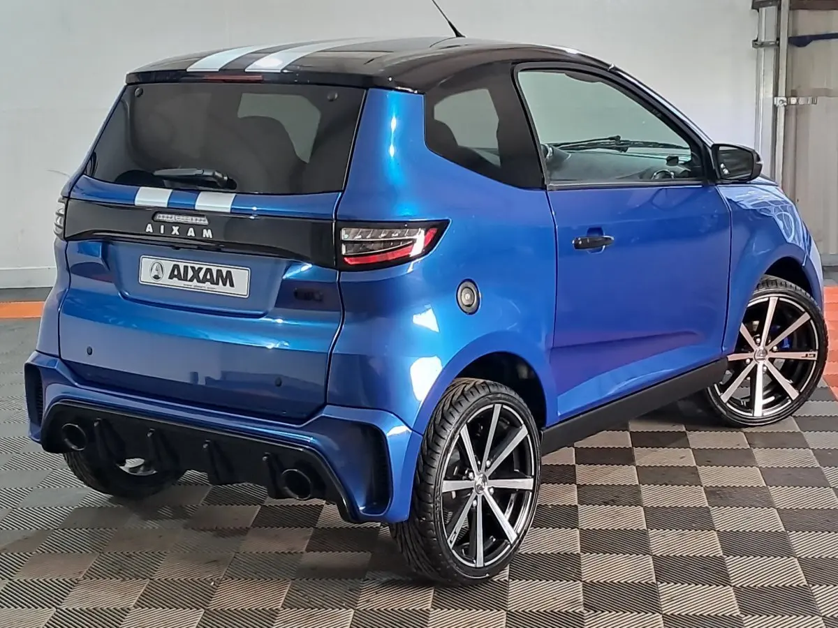 Vue 3/4 arrière droite de l'AIXAM AMBITION bleu 2026 avec jantes noires et bandes blanches sur le toit.