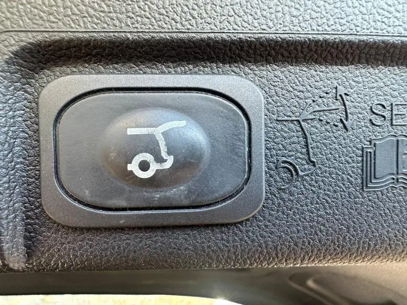 Bouton noir de commande d'ouverture du hayon sur tableau de bord texturé d'un Ford Puma 2024 gris Solar métallisé.