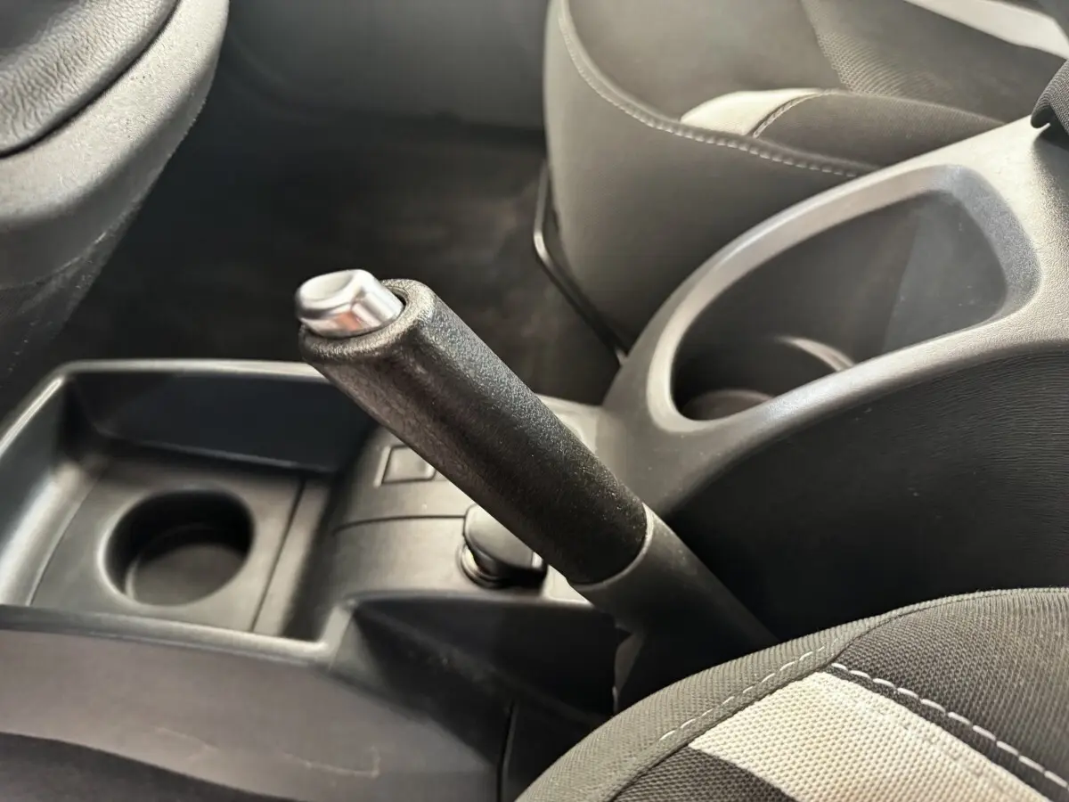 Gros plan intérieur sur le frein à main et porte-gobelets entre les sièges avant noirs du Renault Kangoo blanc.