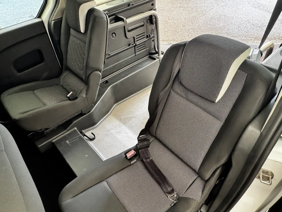 Vue intérieure sur les sièges arrière gris foncé du Renault Kangoo Zen blanc, avec banquette fractionnée et ceinture de sécurité.