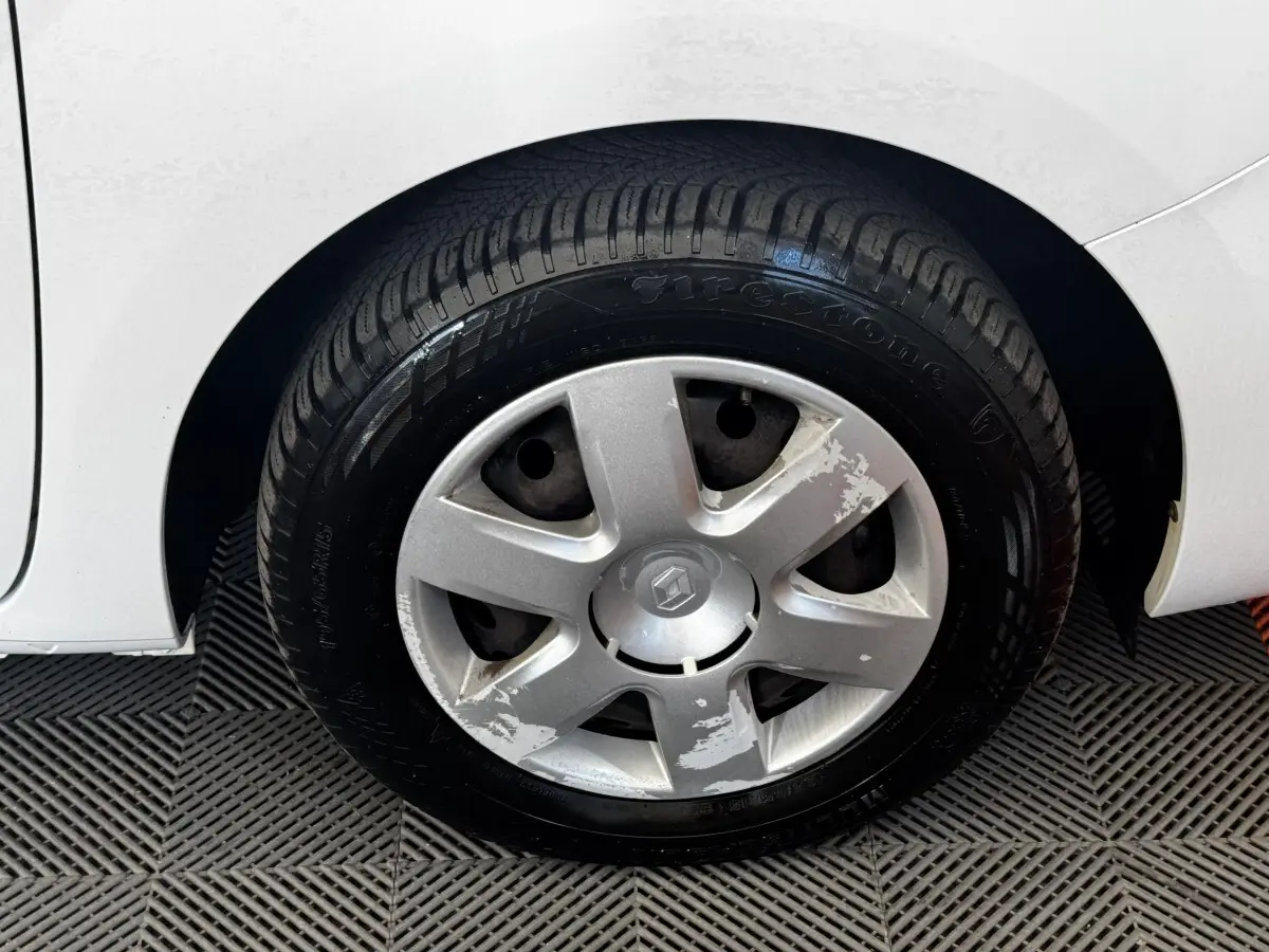 Gros plan sur la roue avant droite blanche d’un Renault Kangoo 2016 avec enjoliveur abîmé et pneu Firestone.