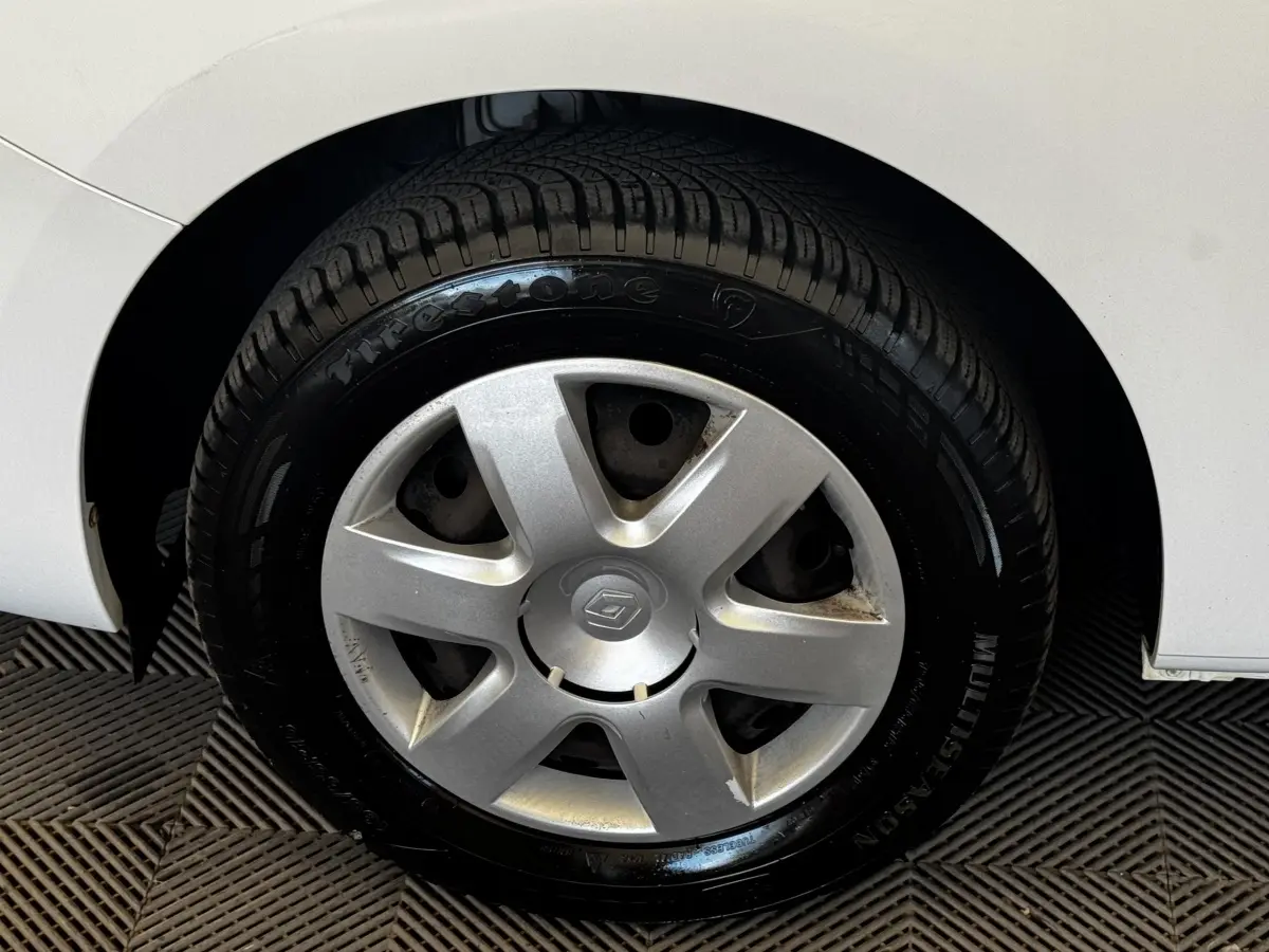 Gros plan sur la roue arrière droite d’un Renault Kangoo blanc, montrant le pneu Firestone et l’aile du véhicule.