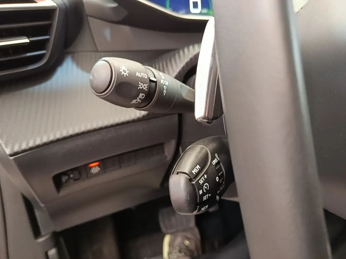 Gros plan sur les commandes de régulateur de vitesse et des phares à gauche du volant d’un Peugeot 2008 blanc, intérieur noir.