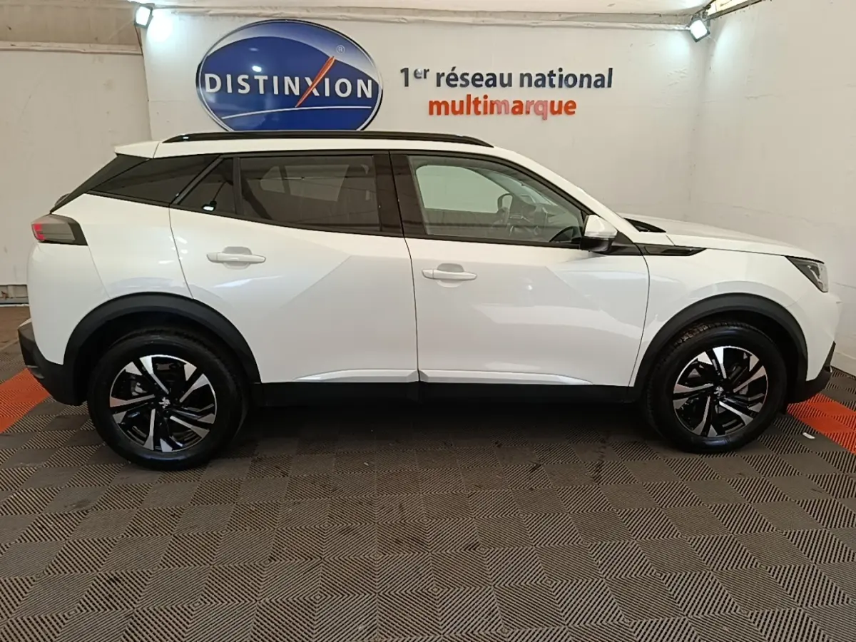 Peugeot 2008 blanc vue de profil côté gauche, avec jantes noires et toit noir contrastant en intérieur showroom.