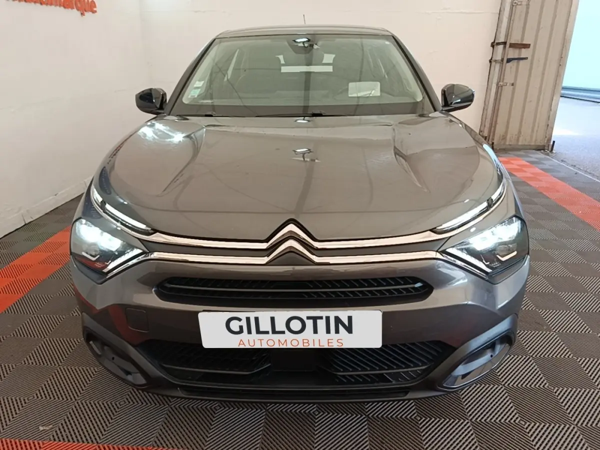 Vue avant d'une Citroën C4 gris clair avec feux LED allumés dans un showroom intérieur.