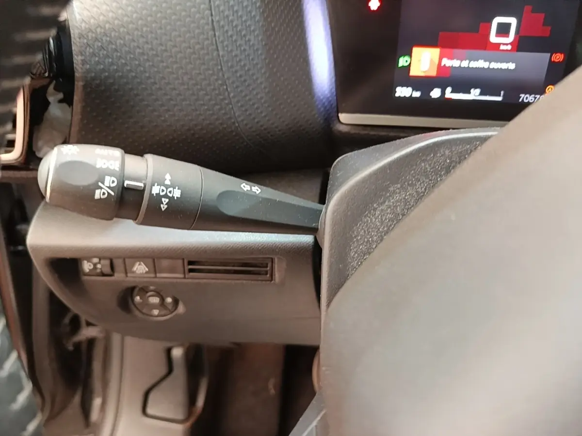 Détail du commodo gauche et partie du volant cuir dans l'habitacle d'une Citroën C4 gris clair, tableau de bord partiellement visible.