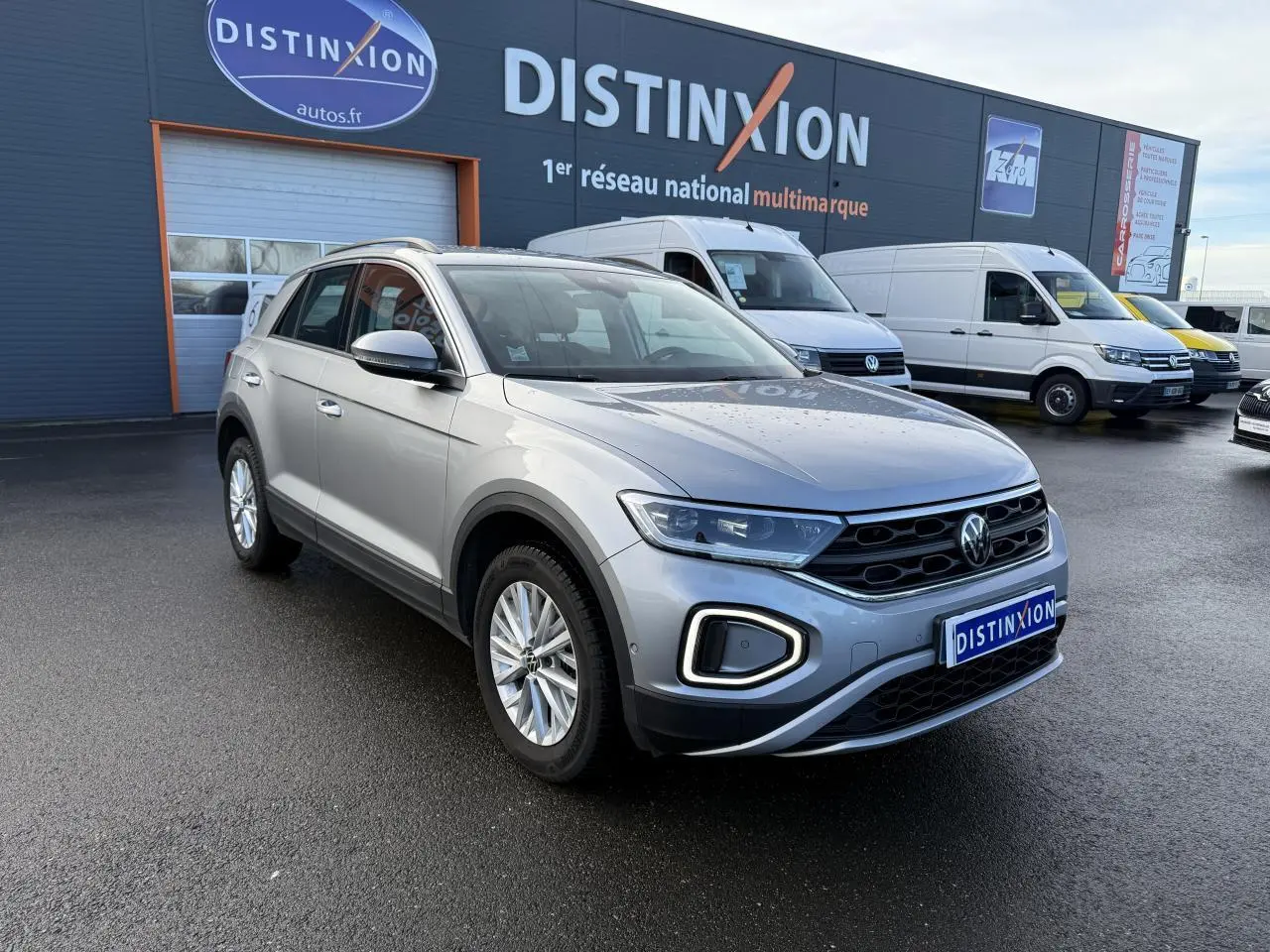 Volkswagen T-Roc gris pyrite en 3/4 avant droit, avec feux LED et calandre noire sur parking extérieur.