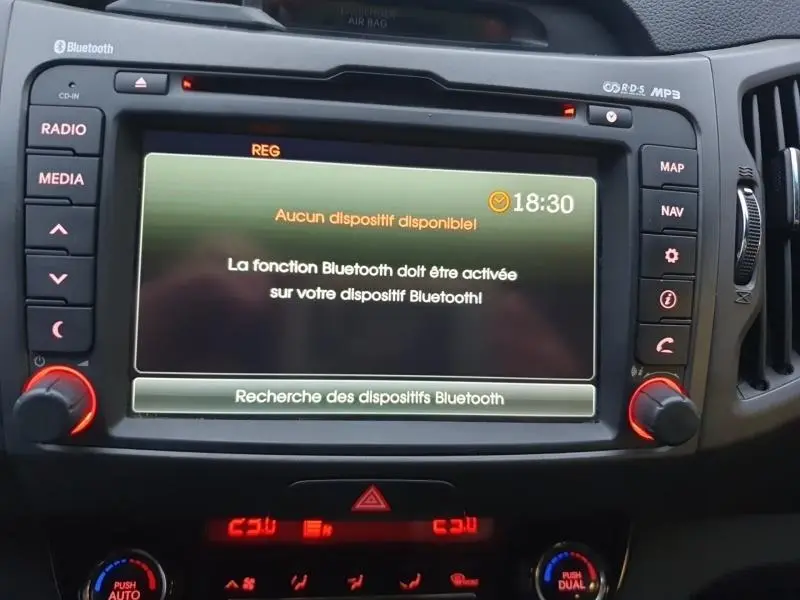 Écran central multimédia du Kia Sportage 2013 affichant un message Bluetooth, entouré de boutons noirs avec éclairage rouge.