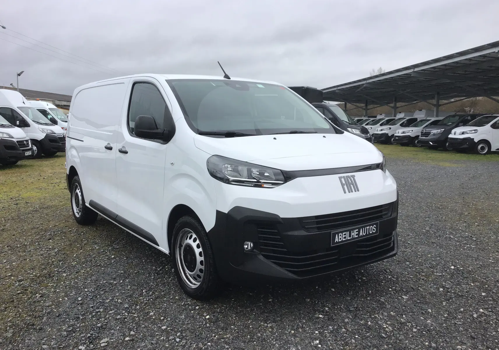 Vue 3/4 avant d’un FIAT Scudo Fourgon blanc 2024 avec pare-chocs noir et jantes acier, sur parking extérieur.