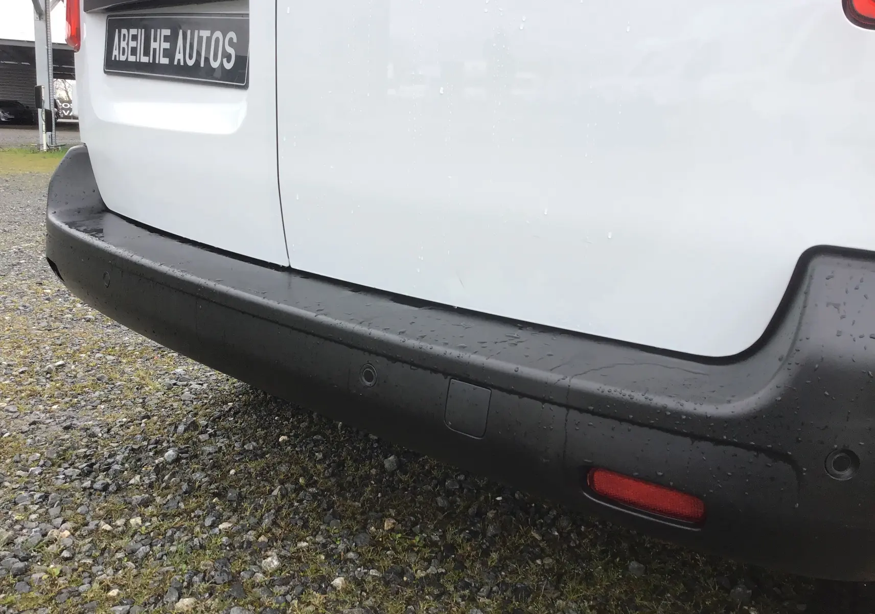 Gros plan sur le pare-chocs arrière noir du FIAT Scudo Fourgon blanc, avec capteurs de recul visibles sous la pluie.