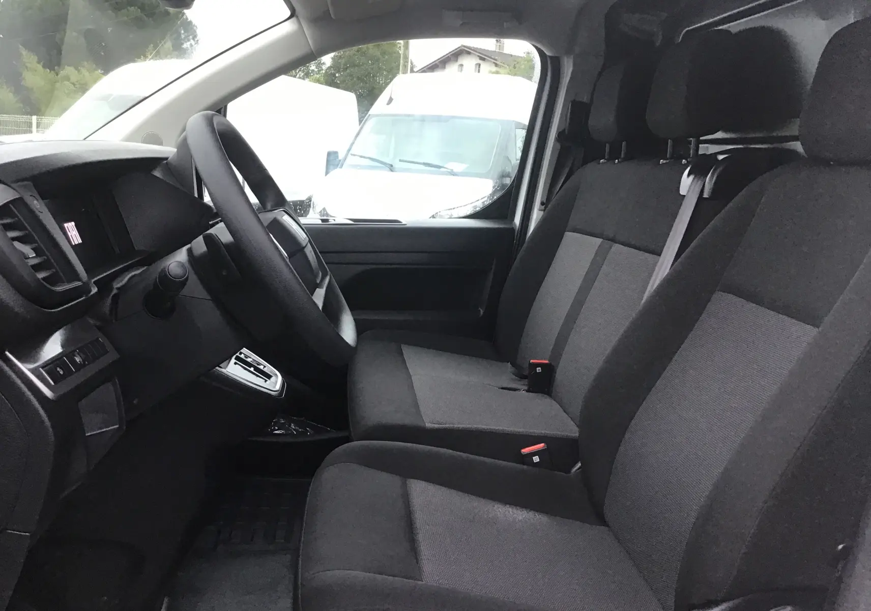 Vue intérieure côté conducteur du Fiat Scudo Fourgon 2024, sièges tissu gris et tableau de bord noir avec volant.