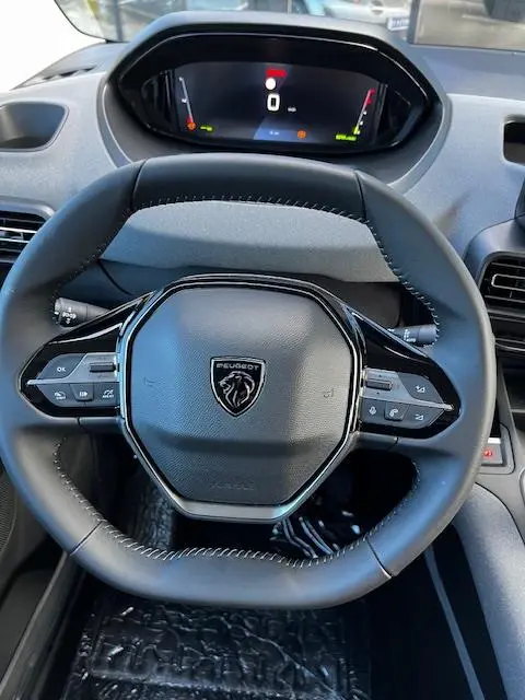 Vue rapprochée du volant cuir noir du Peugeot Rifter 2024 avec tableau de bord digital et commandes intégrées.