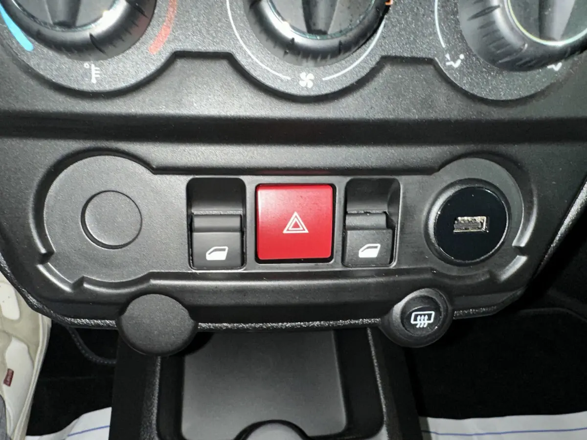 Gros plan sur la console centrale noire de l'AIXAM AMBITION rouge, montrant les commandes de vitres et le bouton de warning rouge.