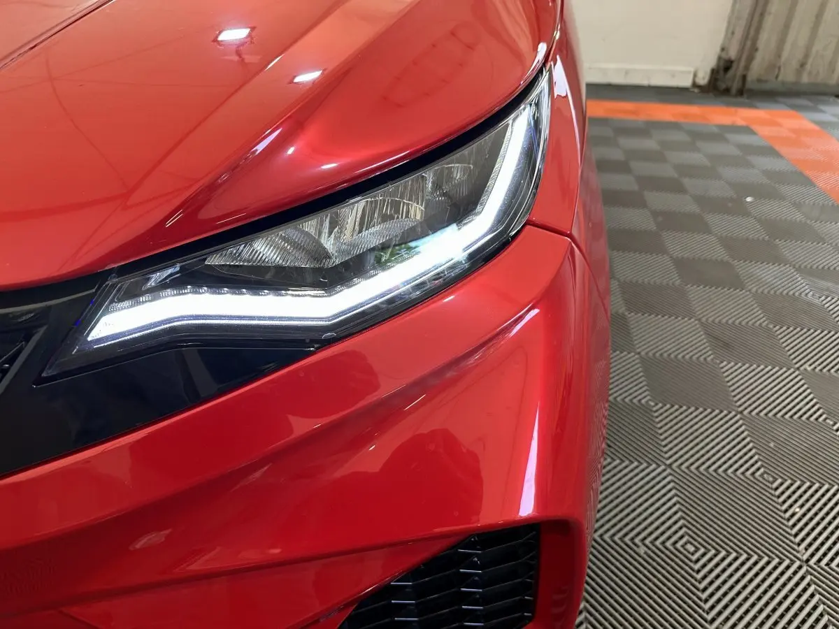 Gros plan sur le phare avant droit allumé d'une Aixam Ambition rouge, avec une partie du pare-chocs visible.