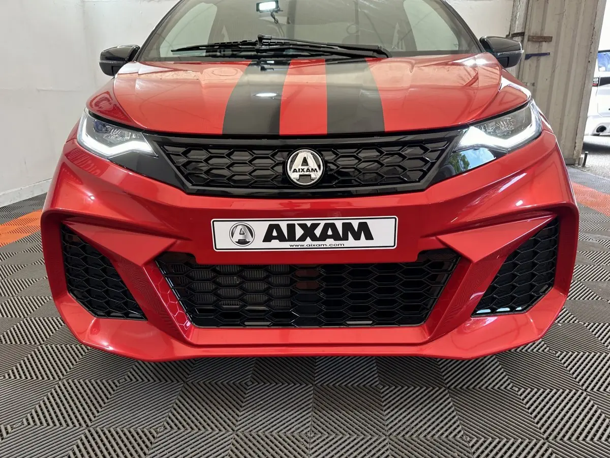 Vue frontale rapprochée de l'AIXAM AMBITION rouge 2026 avec bandes noires et calandre hexagonale distinctive.