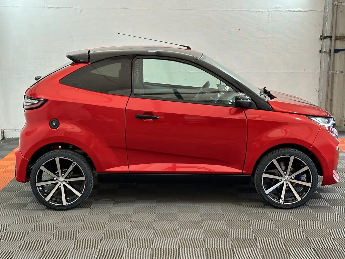 Vue de profil côté gauche d'une Aixam Ambition 0.5 City Coupe GTI rouge avec toit noir et jantes alliage noires.