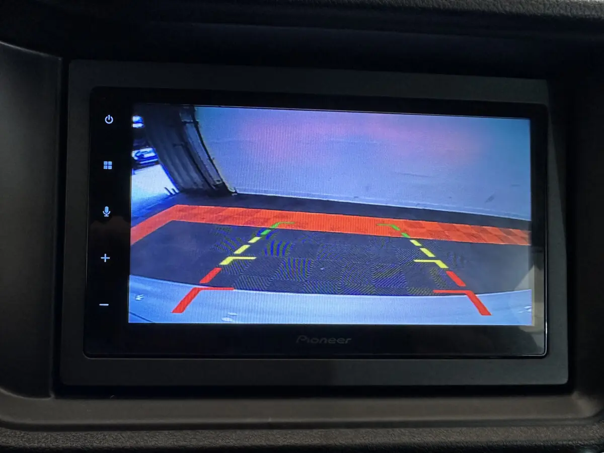 Écran intérieur montrant la caméra de recul avec repères colorés, dans une Aixam Ambition rouge 2026 côté conducteur.