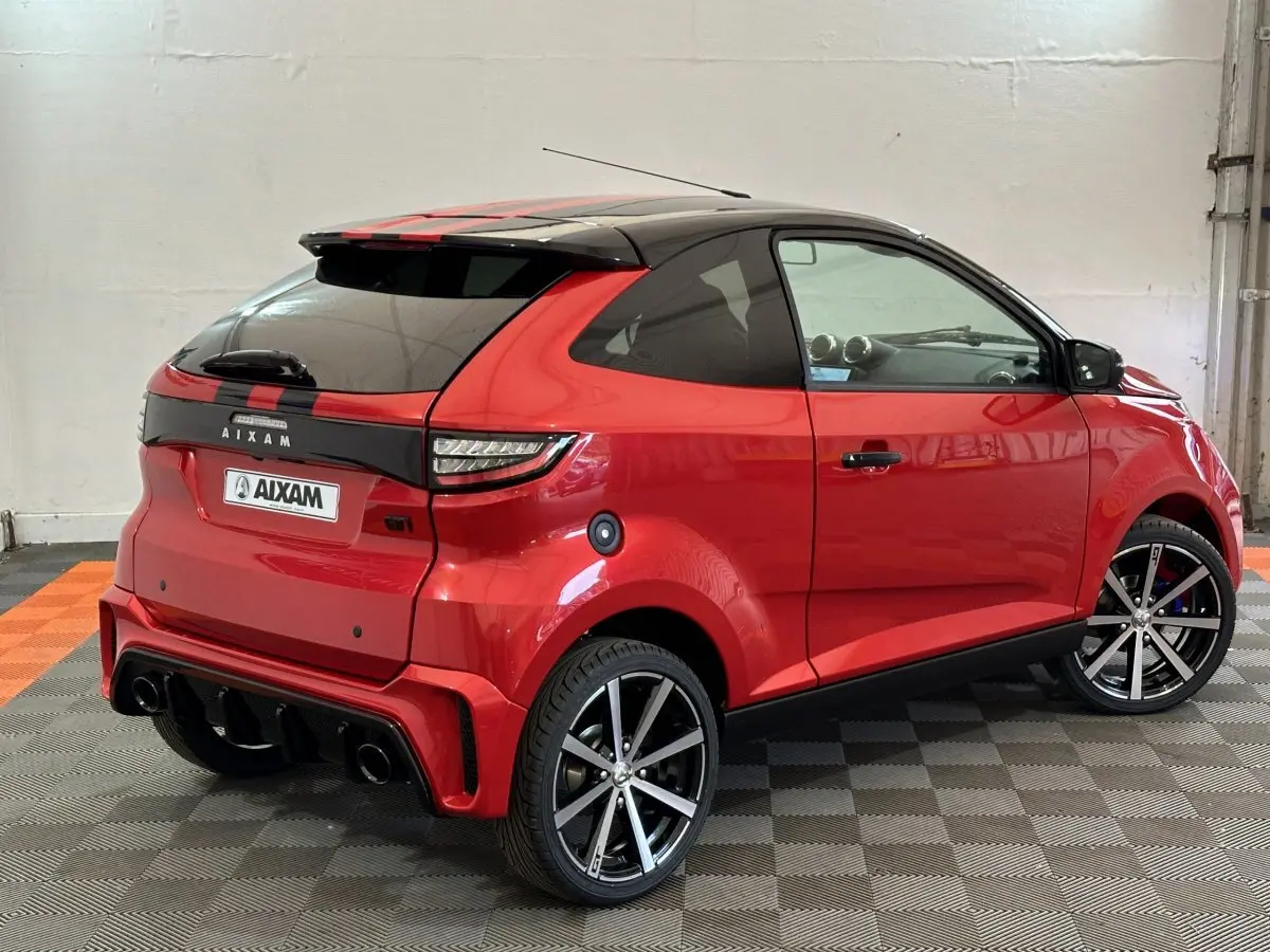 Vue 3/4 arrière droite d'une Aixam Ambition rouge 2026 avec toit noir, jantes alliage et détails sportifs GTI.