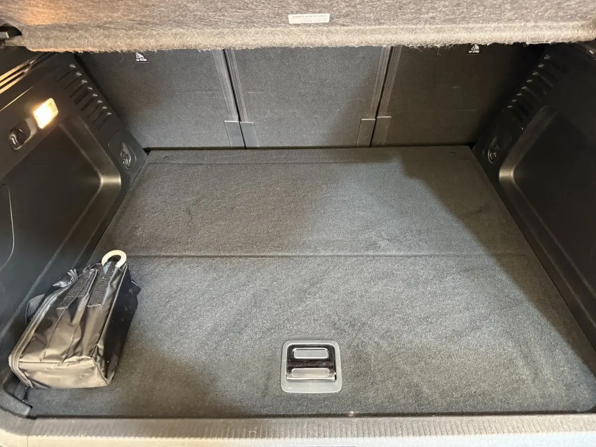 Coffre vu de face d'un Citroën C5 Aircross Hybrid bleu, avec tapis noir et un sac plié à gauche.