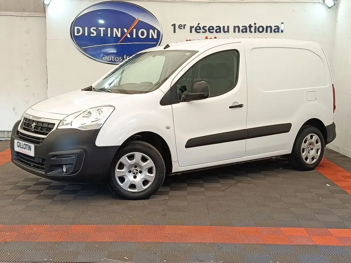 Vue 3/4 avant droit d'un Peugeot Partner blanc 2018 avec pare-chocs noirs et jantes acier en intérieur showroom.