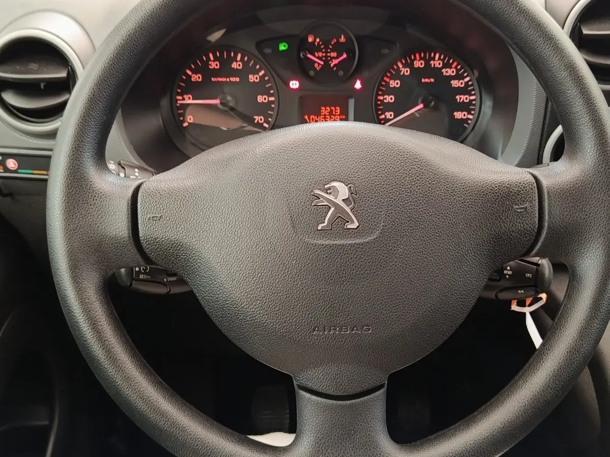 Vue rapprochée du volant noir de Peugeot Partner 1.6 BlueHDi 2018 avec tableau de bord et compteurs rouges en arrière-plan.