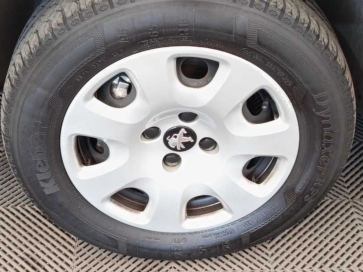 Gros plan sur la roue avant droite avec jante acier blanche et logo Peugeot central visible.
