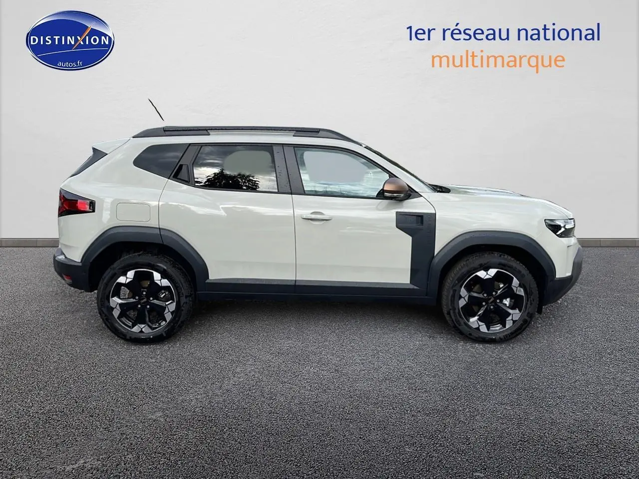 Profil droit du Dacia Duster 2025 couleur Sandstone avec jantes noires et barres de toit visibles.