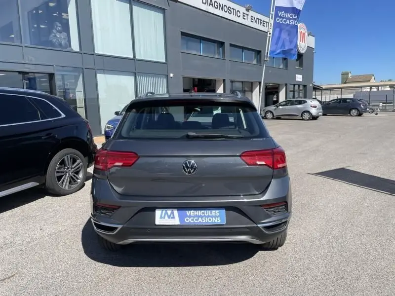 Vue arrière d'un Volkswagen T-Roc gris foncé métallisé 2021, version 1.5 TSI 150 Active DSG7, sur parking de concession.