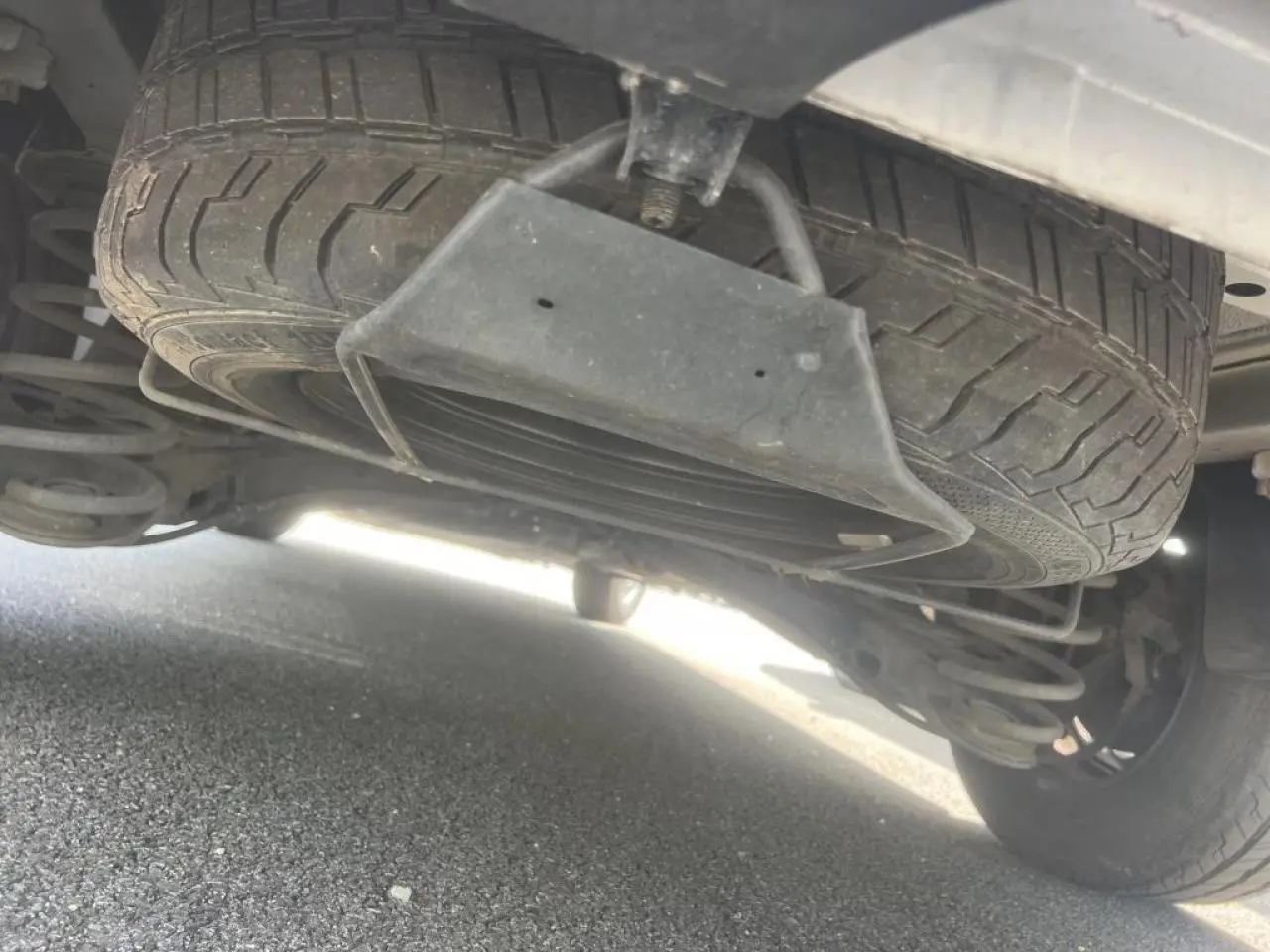 Gros plan sous le Citroën Jumpy blanc montrant la roue de secours suspendue et la suspension arrière.