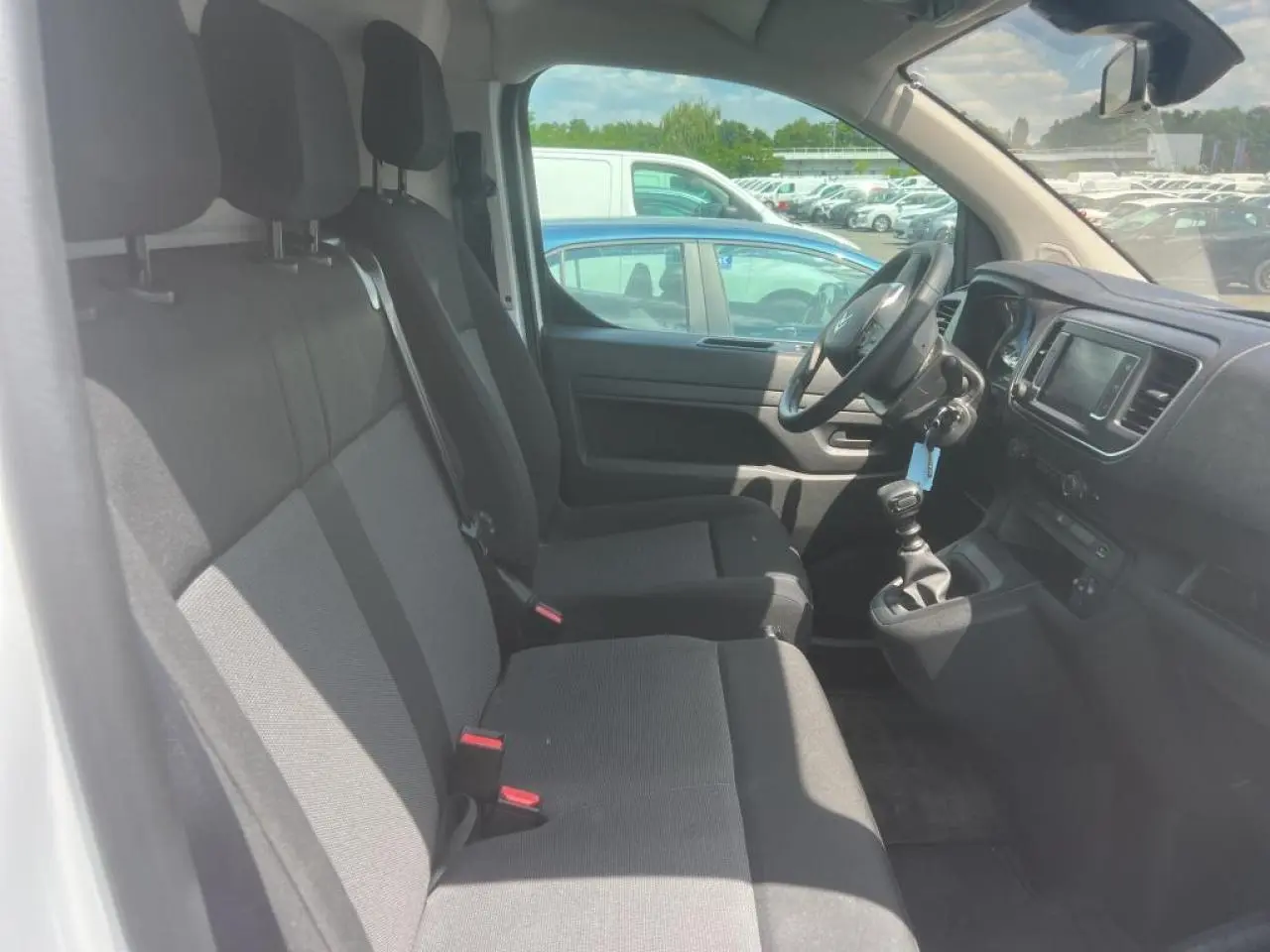 Vue intérieure côté conducteur du Citroën Jumpy XL blanc, montrant les sièges tissu bi-ton et le tableau de bord avec écran tactile.