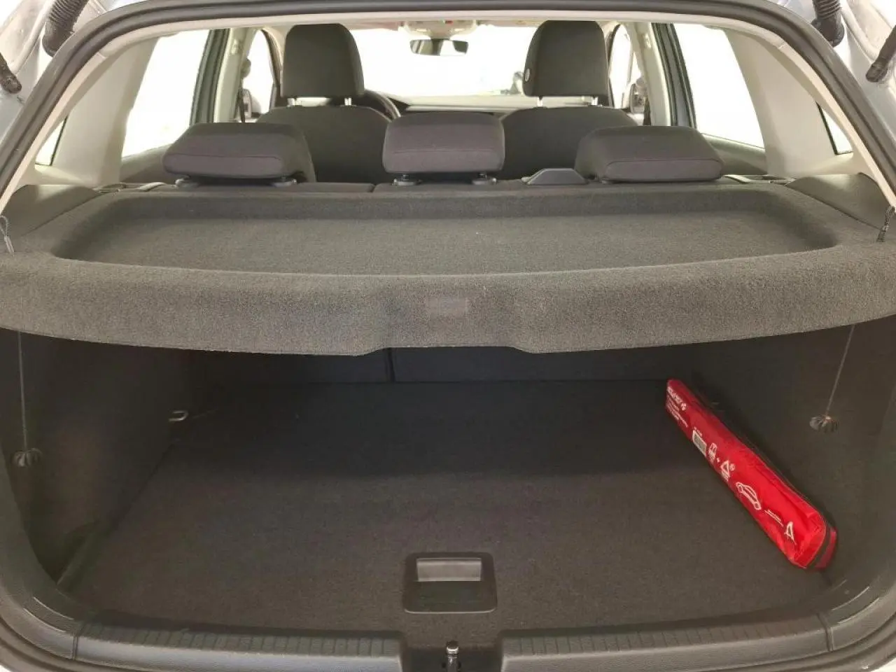Vue arrière du coffre ouvert d'une Volkswagen Polo gris clair, avec cache-bagages et trousse de sécurité rouge sur le côté droit.